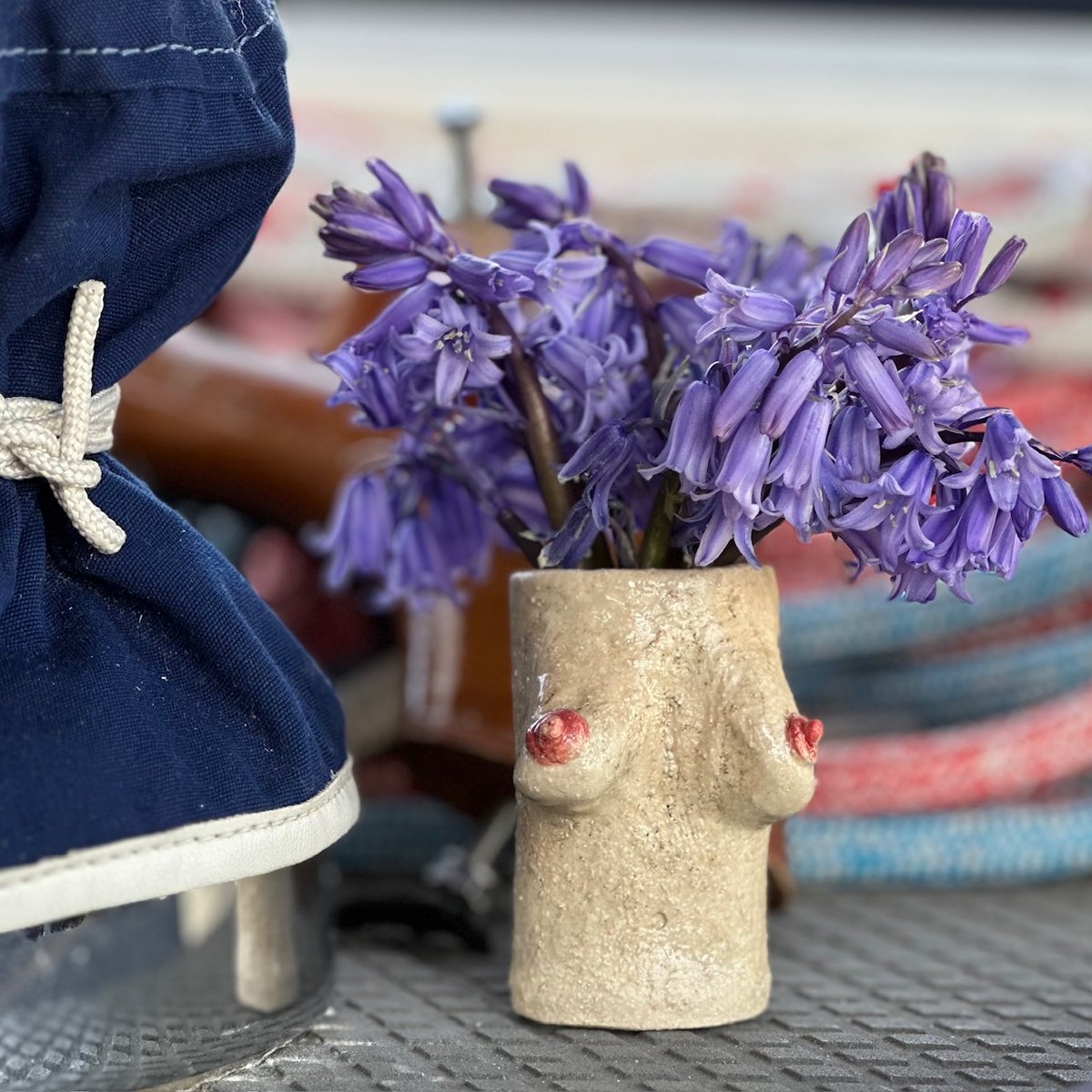 Quirky breast-shaped ceramic vase with purple bluebells on deck - girls, don't forget to check your boobs