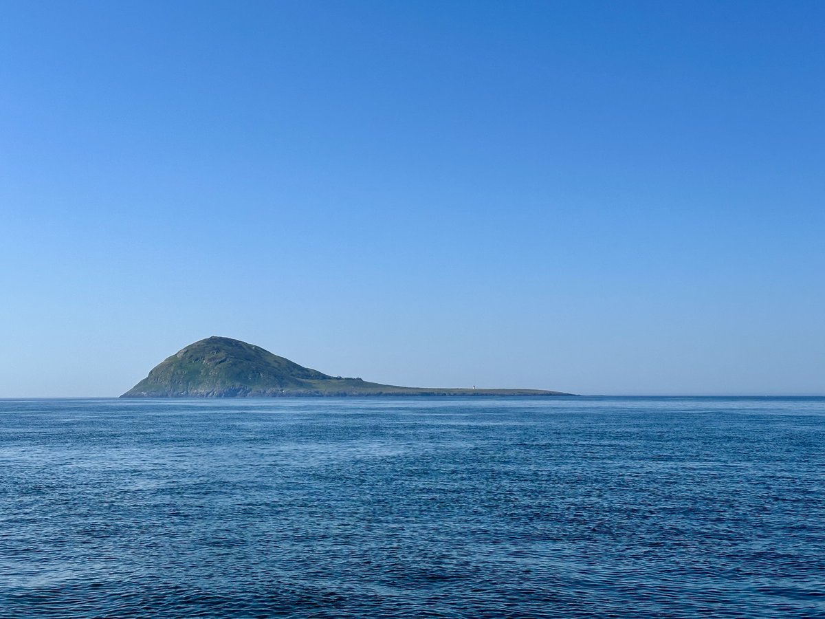 Bardsey Island from the water - the distinctive hill and low peninsula under clear sky