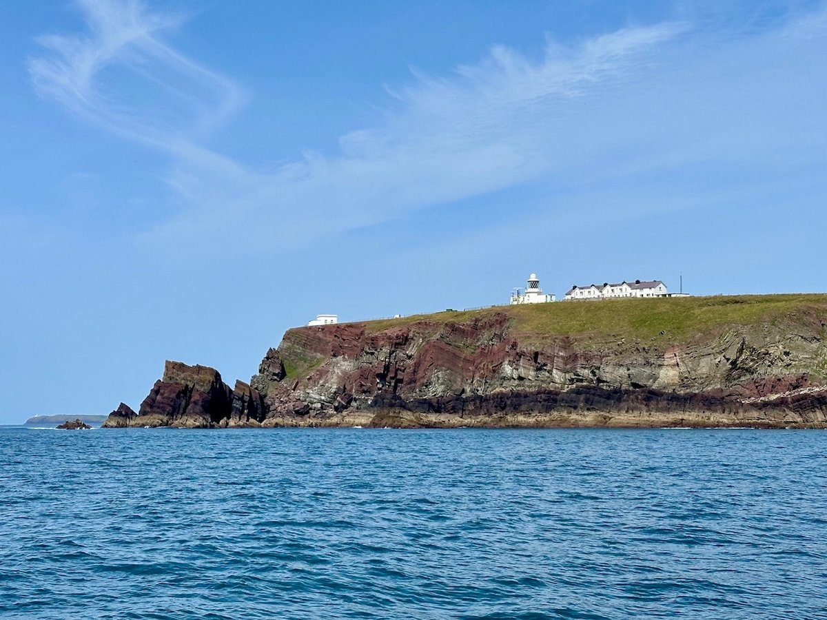 St Anne's Head lighthouse perched on red and green cliffs above a blue sea